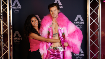 Eine Frau umarmt die Wachsfigur von Harry Styles, die in einem auffälligen, pinken Outfit im Madame Tussauds Berlin ausgestellt ist.