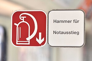 Aufkleber, auch als Piktogramm, verweisen auf den Feuerlöscher und Notfallhammer.